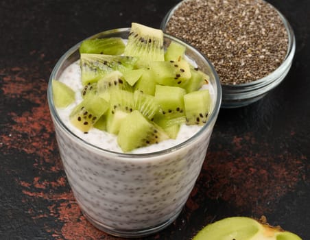 Glass of chia seed pudding mixed with diced kiwi is on a black surface