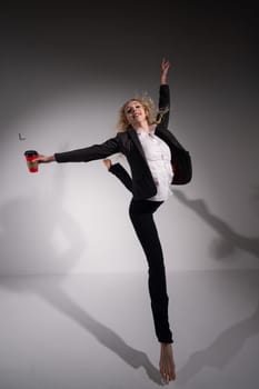 Barefoot ballerina in business suit jumping with a cup of coffee on a white background