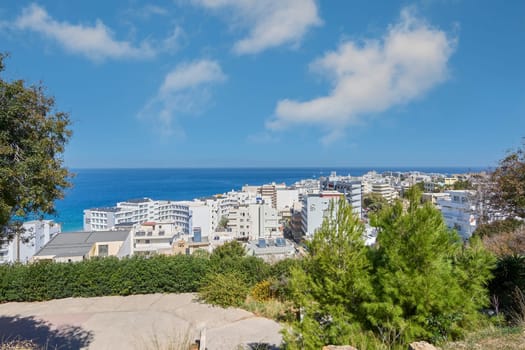 Rodas.Greece - june 07, 2025: Serene and picturesque scene of a Mediterranean resort town, featuring a vibrant mix of traditional and modern buildings under a bright, cloud-dotted sky, overlooking