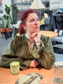 Woman smiling in cafe atmosphere with matcha. Joy, relaxation and mindful presence in everyday life.
