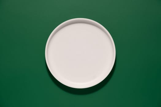 A simple round white plate sits on a vibrant green background, showcasing its smooth surface and unadorned design, ideal for presentations during dining occasions.