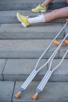Girl with leg injury sits on the stairs with crutches