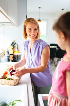 Mother enjoys unpacking fresh produce with her daughter beside.