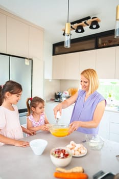 A mother shows her kids how to mix ingredients.