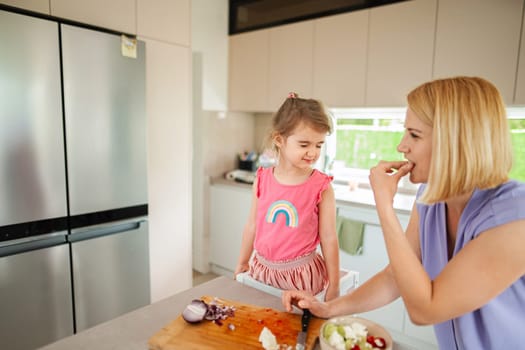 Child enjoys cooking with parent in a bright kitchen.