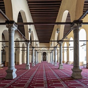 Al-Zahir Baybars Mosque in Cairo, a testament to Egypt's profound Islamic heritage, characterized by its towering columns, arched passages, and intricately decorated prayer carpet