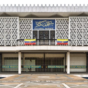 Facade of the National Mosque (Masjid Negara) with Malaysian flags, a modern Islamic architectural landmark in Kuala Lumpur, Malaysia