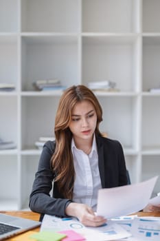 An asian businesswoman reviews paperwork reports at her office workplace..