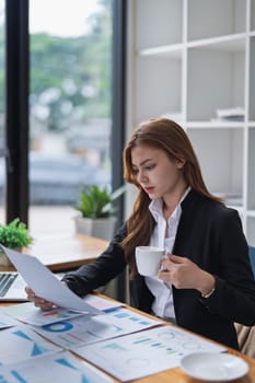 Professional woman reviews financial reports with coffee at her office desk..