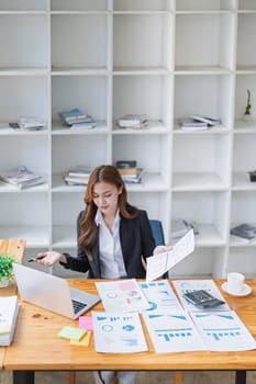 Successful young businesswoman works with graphs at her bright office desk..