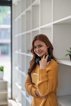 Smiling young woman holds a book in front of a white bookshelf indoors..