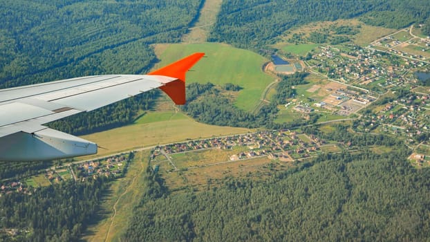 Airplane wing hovering above verdant countryside, revealing patchwork villages nestled amid lush forest landscape during daytime flight