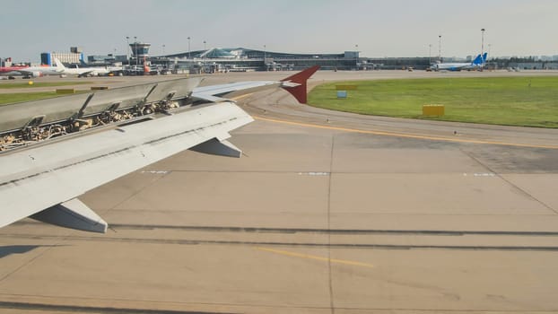 Airplane is landing at airport terminal with open flaps on wing and other aircraft taxiing in background