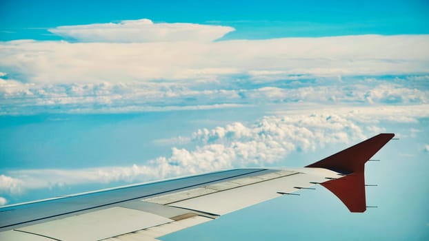 Wing of an airplane flying above a layer of white clouds, with a clear blue sky in the background