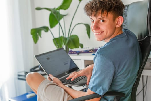 Teenager with a laptop, a fourteen-year-old boy with a laptop in his hands sits at a computer desk, turns around and smiles contentedly. High quality photo