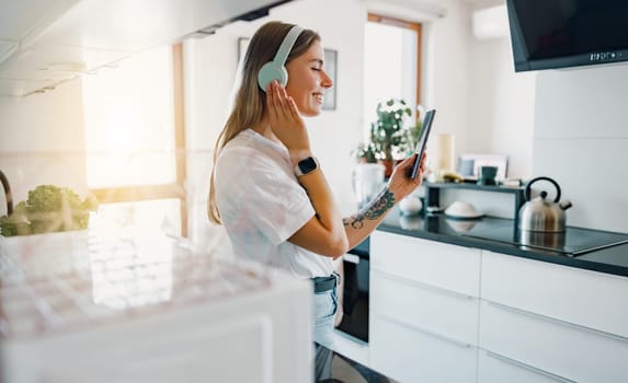 A woman with headphones is engaged with her tablet in a stylish kitchen, showcasing a modern lifestyle
