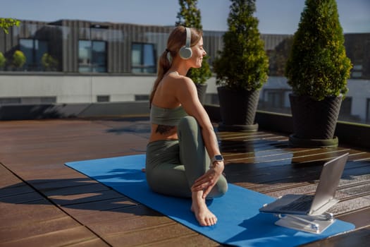 A focused woman practicing yoga outdoors on a sunny rooftop, harmoniously blending relaxation and modern technology