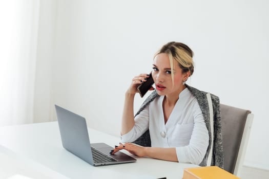 Business woman sitting at office desk with laptop and talking on phone