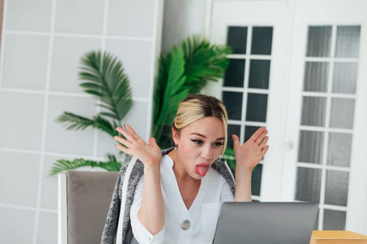 Business woman sitting at office desk with laptop and sticking out her tongue