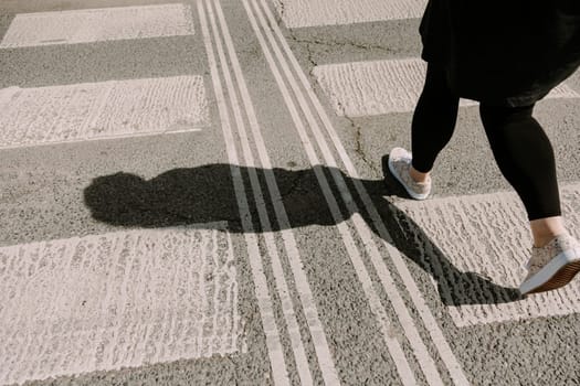 A woman confidently striding over a city crosswalk, captured from behind in bright sunlight. Perfect for themes of personal journey, direction, motivation, and lifestyle in urban settings