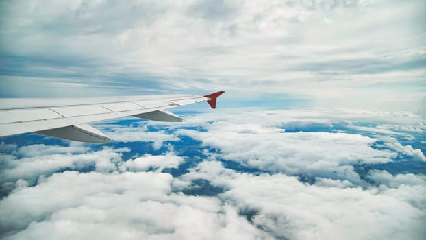 Airplane wing soaring through cloudy sky, offering a breathtaking view of the earth below