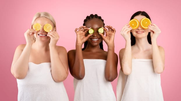 Beauty And Skin Care. Three Diverse Women In Bath Towels Covering Eyes With Cucumber And Orange Slices, Making Organic Face Masks, Posing Together Over Beige Studio Background, Copy Space