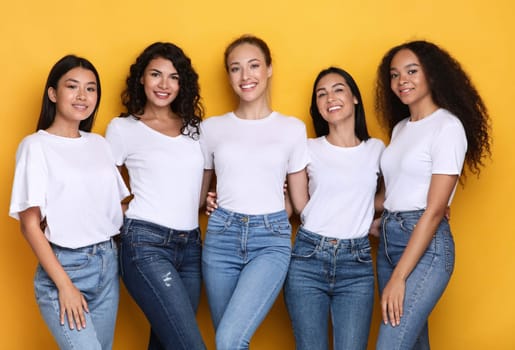 Group Of Five Diverse Models Ladies Posing Smiling To Camera Standing On Yellow Studio Background. Mixed Women Expressing Positive Emotions. Female Beauty And Diversity Concept