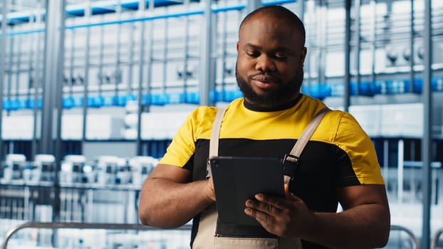 Smart factory engineer oversees operation of robotic arms and assembly lines on facility floor. Industry 4.0 plant african american man monitors system performance and troubleshoots issues, camera A