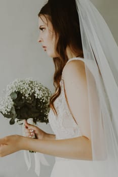 Portrait of one beautiful young Caucasian recognizable brunette bride holding a bouquet of white boutonnieres and waving her arms with serious emotion on her face, bottom view close up with selective focus.