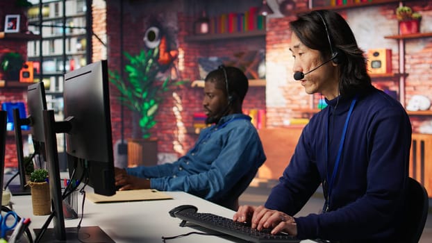 Call center senior agent dealing with unhappy customers, listening to issues. Experienced Asian customer support worker handling clients complaints in company workspace, camera B