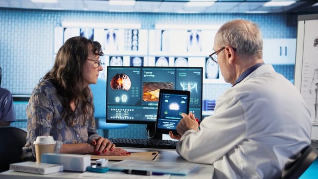 Male general practitioner explaining preventative medicine and risk factors when it comes to cancer, reviewing MRI scans. Medic and woman patient exploring treatment options. Camera A.