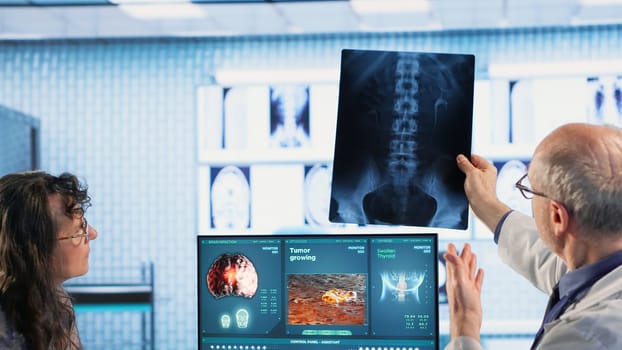 Oncology consultation takes place as a senior medic explains radiology scan, emphasizing preventive medicine and healthy lifestyle recommendations. Shares risk factors and causes. Camera B.