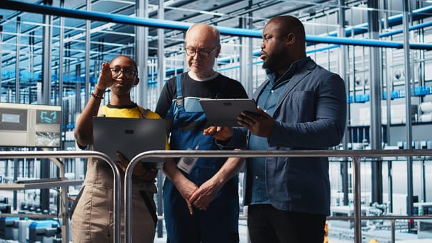 Engineers talking with manager overseeing smart factory, showing collected metrics. Technicians receiving feedback from supervisor in industry 4.0 industrial plant equipped with sensors, camera A