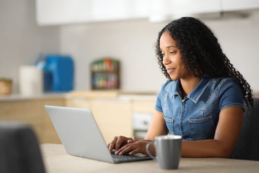 Black woman in a kitchen using laptop at home