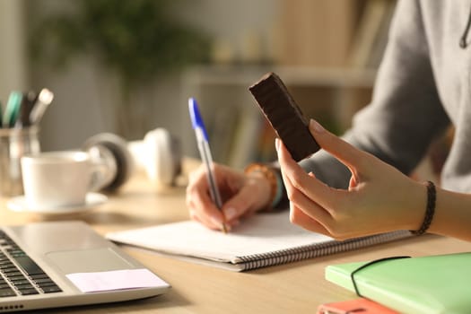 Close up portrait of a student in the night taking notes holding chocolate bar