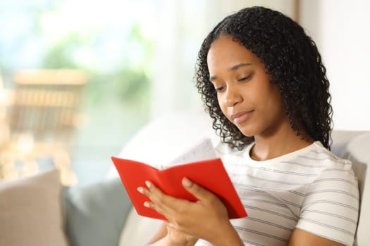 Black woman is handwriting in paper agenda sitting in a couch at home