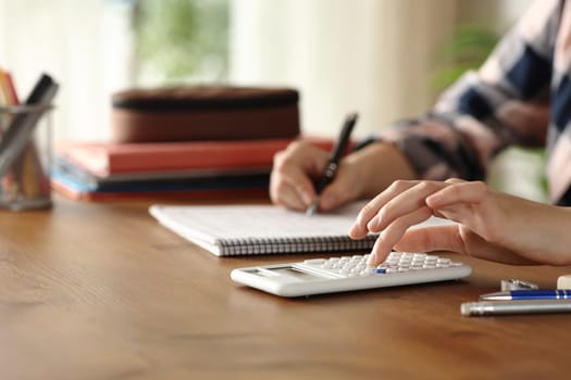 Close up of a student hand using scientific calculator and taking notes at home