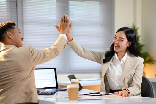 Happy business partners giving a high five in celebration of success at the office.