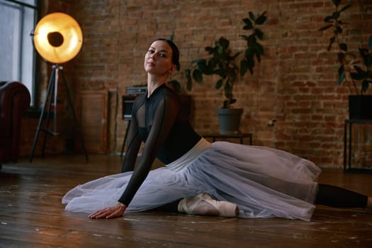 Ballerina is gracefully performing an elegant split in a stylish home studio that is filled with plants