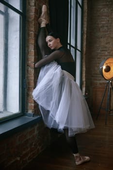 Graceful ballerina elegantly stretches her body against a textured wall in a serene and calming dance studio