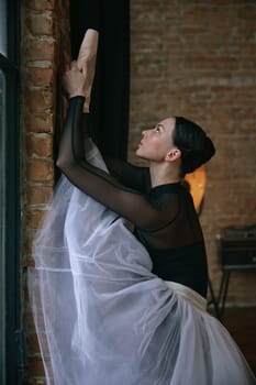 A graceful ballerina elegantly stretches her body against a textured wall in a serene and calming dance studio