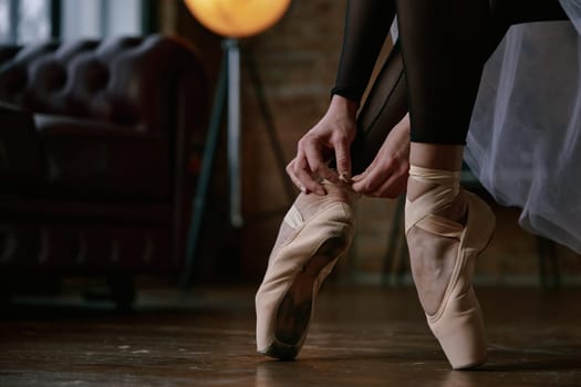 Crop shot of ballerina is gently and delicately wearing her ballet shoes inside a beautifully stylish studio ambiance