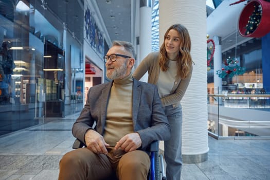 Beautiful woman gently pushes a man in wheelchair along a long hallway, filled with soft light