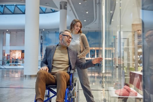 Man in wheelchair navigating through a bustling mall filled with various shops and stores around him