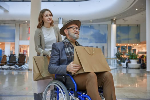 Man who in wheelchair receiving assistance from woman while they are navigating through a shopping mall together
