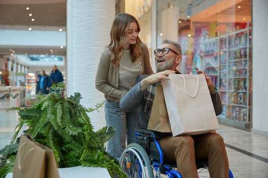 A man who in wheelchair receiving assistance from woman while they are navigating through a shopping mall together