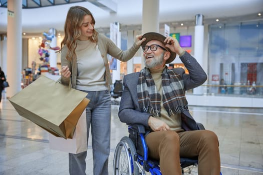 Male person in wheelchair is receiving assistance from a woman while navigating through a shopping mall together