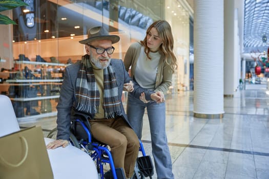 A man with disabilities in wheelchair receiving assistance from a lady navigating through a shopping mall together