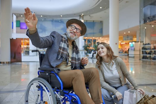 A man who uses a wheelchair is sitting comfortably next to a woman who is holding several shopping bags in her hands