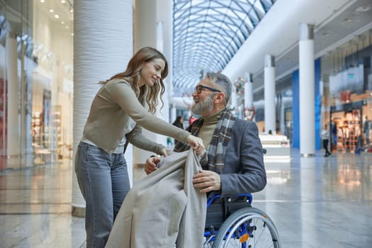 Lady gently placing soft blanket over man in wheelchair to keep him warm and comfortable during their outing together